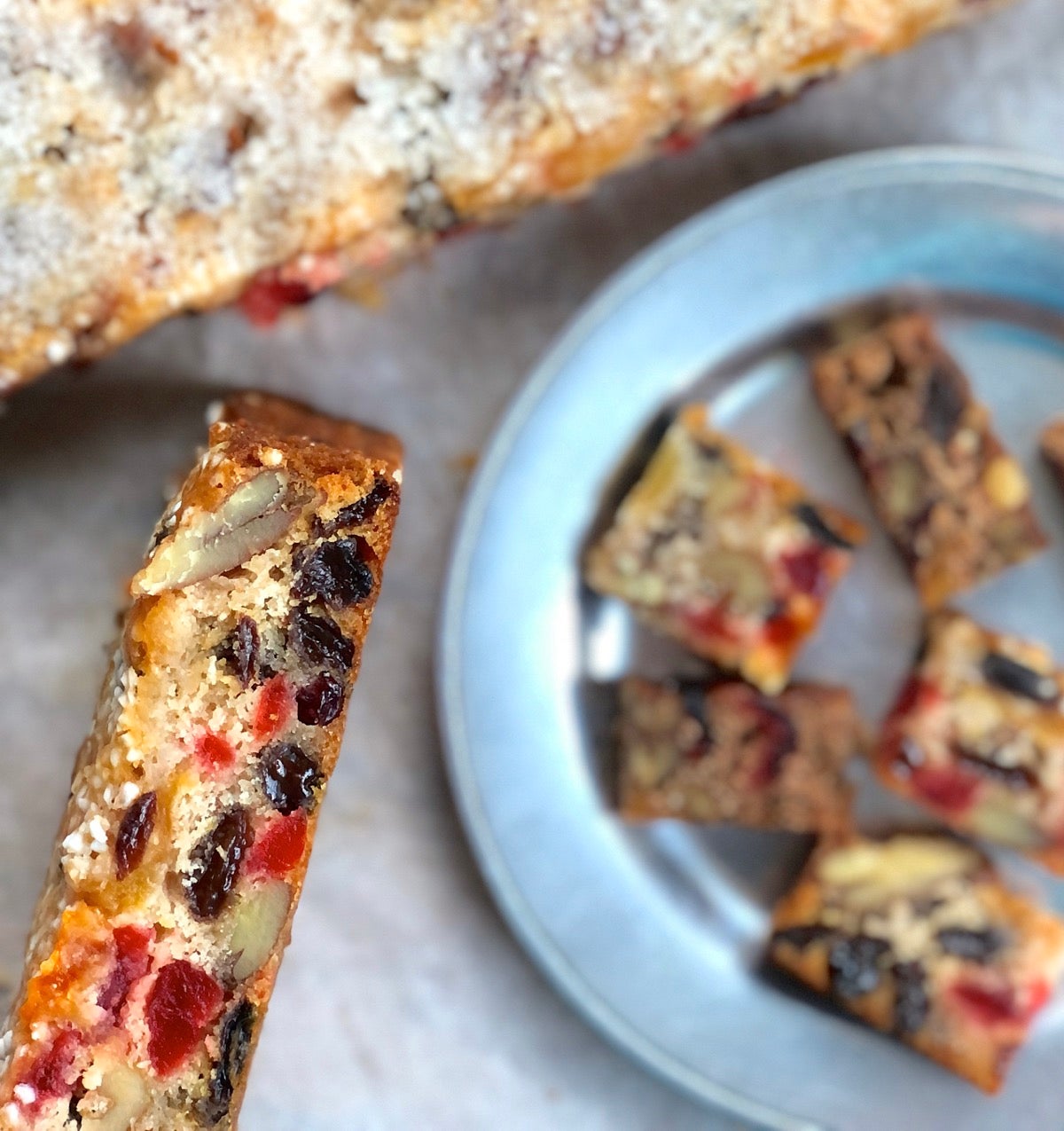 Light fruitcake partially sliced into bars, some on a plate.